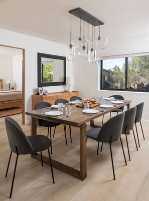 Ein stilvolles Esszimmer mit Holztisch, sechs Stühlen, einer Chandelierleuchtre und einem Spiegel, mit Blick ins Freie.