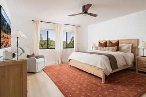 Ein Schlafzimmer mit Bett, Schreibtisch, Stuhl, Deckenventilator und großen Fenstern.