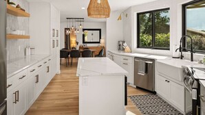 A modern kitchen with white cabinetry, a central island, and a dining area with a wooden table and chairs. - Peaceful Pool and Tub Bliss with Majestic Thunder Mountain Views (Sedona)