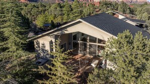 A modern house with a large glass window, surrounded by trees and mountains. - Peaceful Pool and Tub Bliss with Majestic Thunder Mountain Views (Sedona)