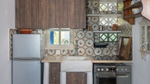 A compact kitchen with wooden cabinets, a built-in oven, and a window. - Liva Mare Serifos (Serifos)
