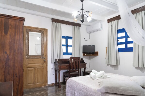 A hotel room with a wooden desk, a bed with rolled towels, a television, and a chandelier. - Liva Mare Serifos (Serifos)
