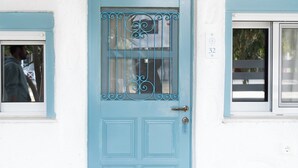 A blue door with a window and a ship's wheel decoration above it. - Liva Mare Serifos (Serifos)
