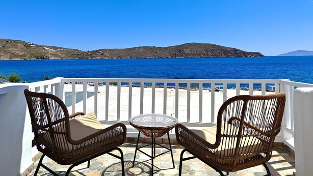 A balcony with two wicker chairs and a small table, overlooking a clear blue sea and distant hills. - Liva Mare Serifos (Serifos)