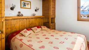 Un dormitorio con estructura de madera, una cama, un estante de pared con adornos y una ventana con vistas a un paisaje nevado.