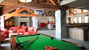 Una mesa de billar en una habitación con sillas rojas, una chimenea y vigas de madera.