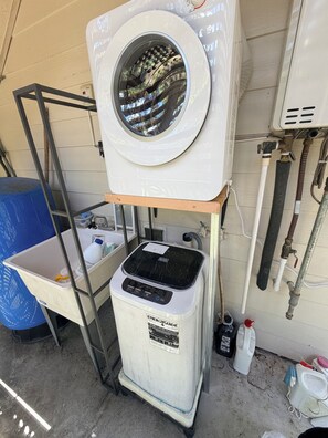 A laundry facility with a washing machine, a dryer, and a metal rack. - Great for nature lovers quiet and calm. Auto gat, security cameras. (Keaau)