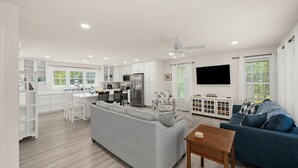A modern kitchen with white cabinets, a dining area with a gray sofa, and a living room with a blue sofa. - Creature Comforts (Rehoboth Beach)