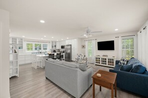 Una cocina moderna con armarios blancos, un área de comedor con un sofá gris y una sala de estar con un sofá azul.