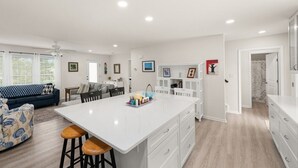 A modern kitchen with a central island, white cabinetry, and a dining area with a blue sofa. - Creature Comforts (Rehoboth Beach)