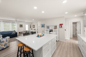 Una cocina moderna con una isla central, armarios blancos y un comedor con un sofá azul.