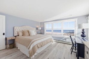 A bedroom with a bed, bedside table, lamp, and a view of the sea through a window. - Sun-Drenched Coastal Escape on Kennebunk Beach (Kennebunk)