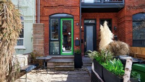 A brick building with a green door, a small outdoor seating area with a bench and table, and a planter with plants. - Downtown Toronto row house. Close to Ossington, Trinity Bellwood & BMO field. (Toronto)