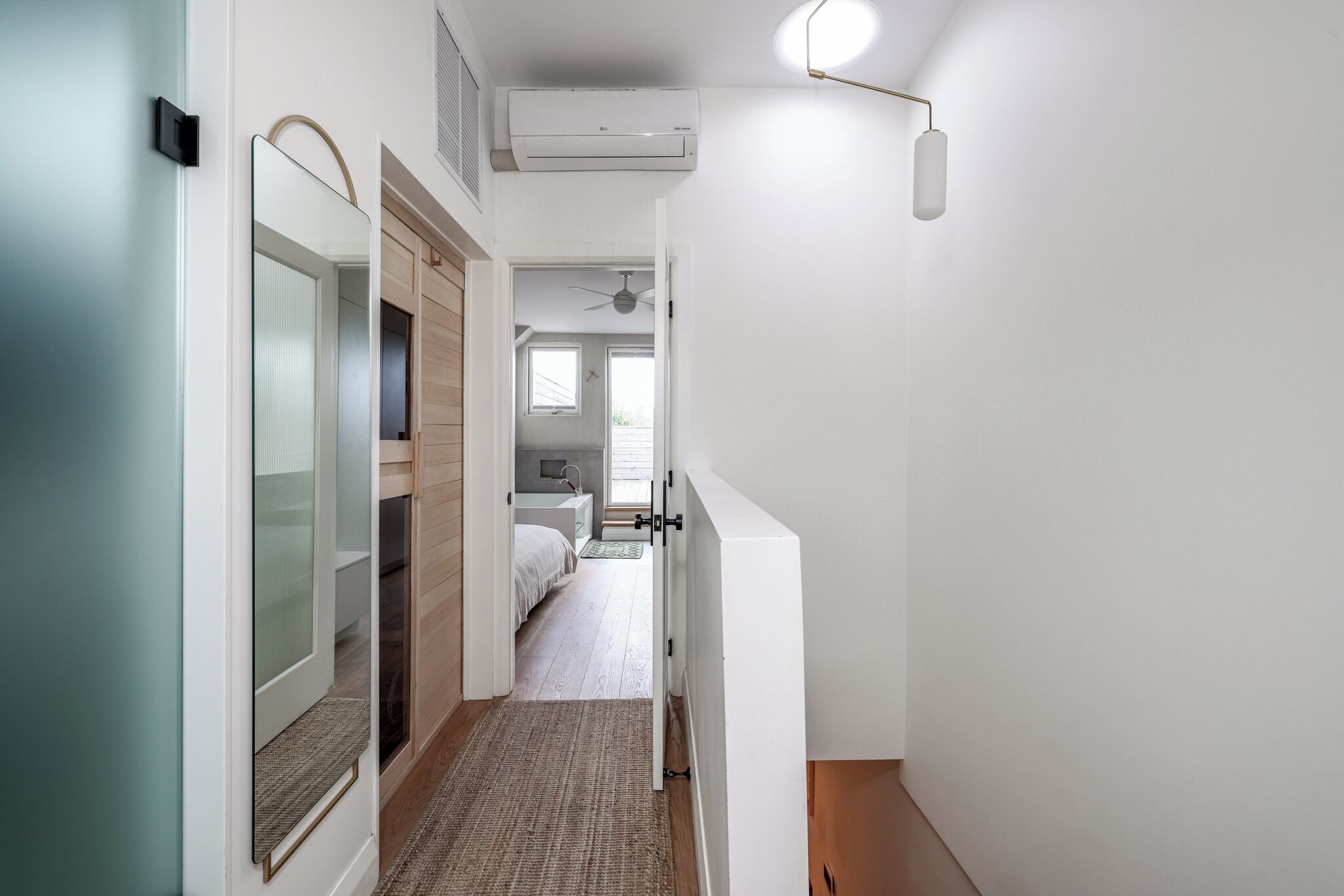 Ein schmaler Flur mit einer Tür, die in ein Schlafzimmer mit Bett und Deckenventilator führt.