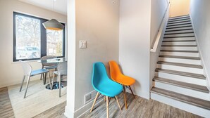 A modern interior with a dining area, two chairs, a staircase, and a window with a view. - Private 3BR Residence | Modern Condo near U of M Stadium | Sleeps 6 (Ann Arbor)