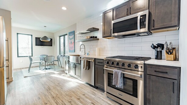 A modern kitchen with stainless steel appliances, wooden cabinets, and a dining area with a glass table and chairs. - Private 3BR Residence | Modern Condo near U of M Stadium | Sleeps 6 (Ann Arbor)