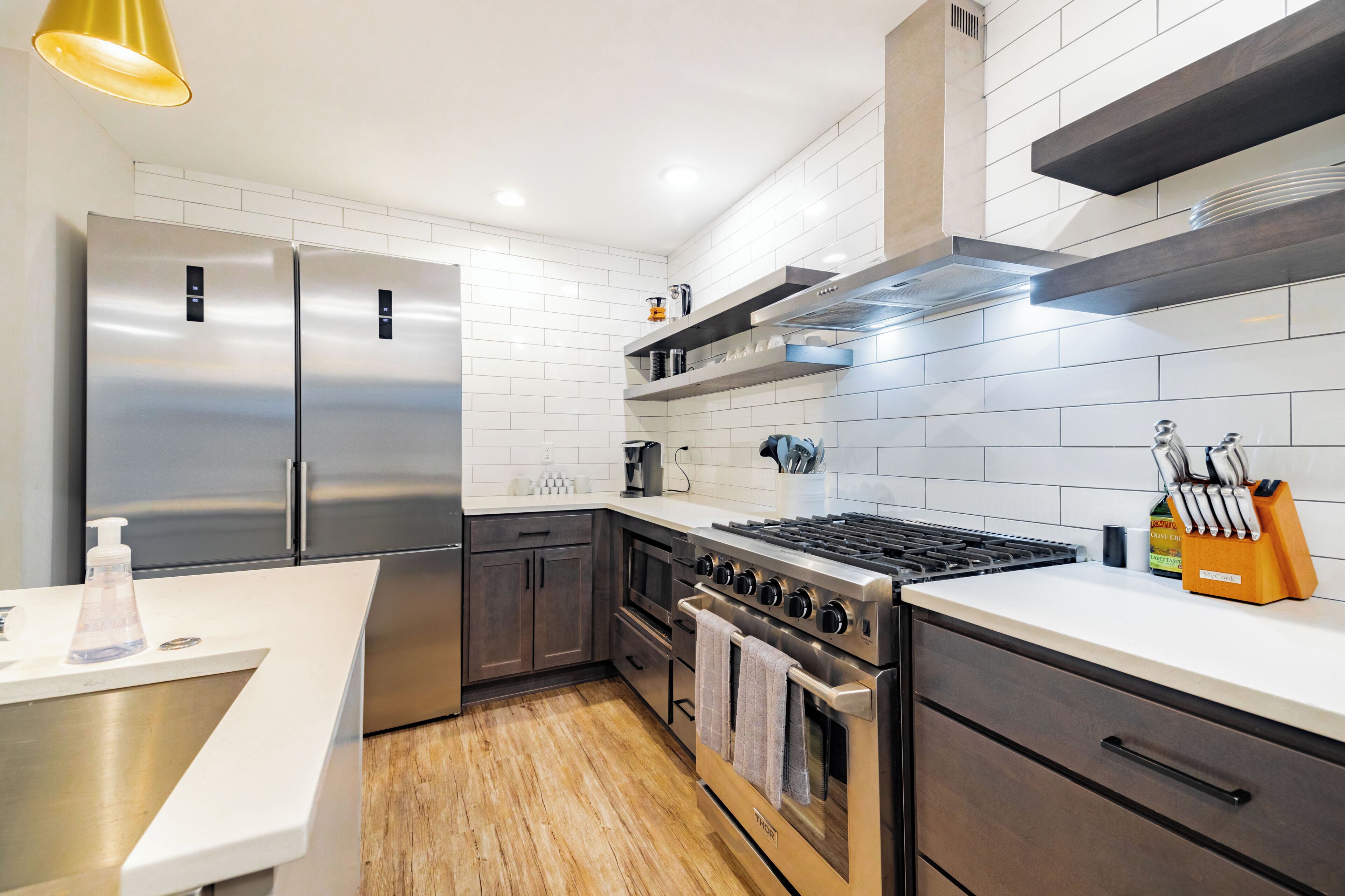 Une cuisine moderne dotée d’appareils électroménagers en acier inoxydable, de murs recouverts de carreaux blancs et d’un plancher en bois.