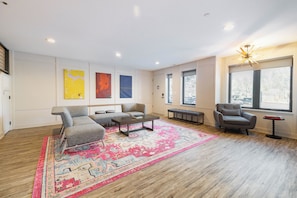 A spacious living room with a large rug, multiple seating options, and artwork on the walls.