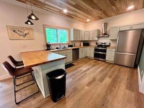 A modern kitchen with a wooden island, stainless steel appliances, and a window providing natural light. - Stepping Stone - Private, Hot Tub, Pet Friendly (Campton)