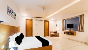 A hotel room with a bed, bedside table, lamp, air conditioning unit, ceiling fan, TV, and a window with curtains. - Deluxe Veridian inn (Lucknow)