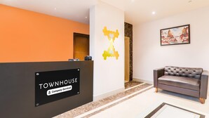 A reception area with a sign reading 'TOWNHOUSE Company-Service,' a couch, and a wall with a geometric art piece. - Deluxe Veridian inn (Lucknow)