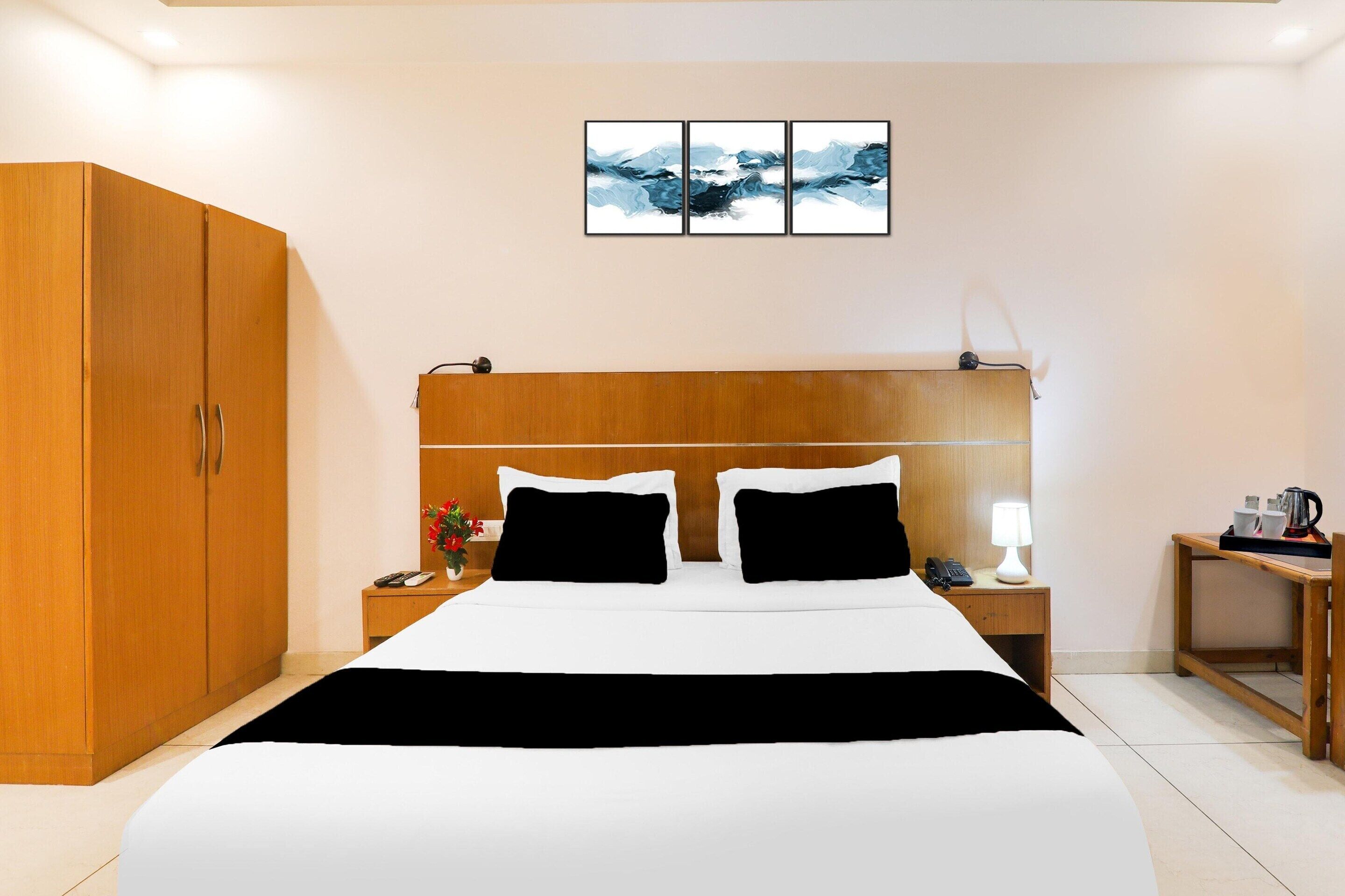 A hotel room with a large bed, wooden wardrobe, bedside tables, a nightstand, and a wall-mounted artwork.