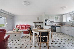 Une cuisine moderne avec des meubles blancs, un coin repas doté d’une table ronde et de chaises, et un canapé en cuir rouge.
