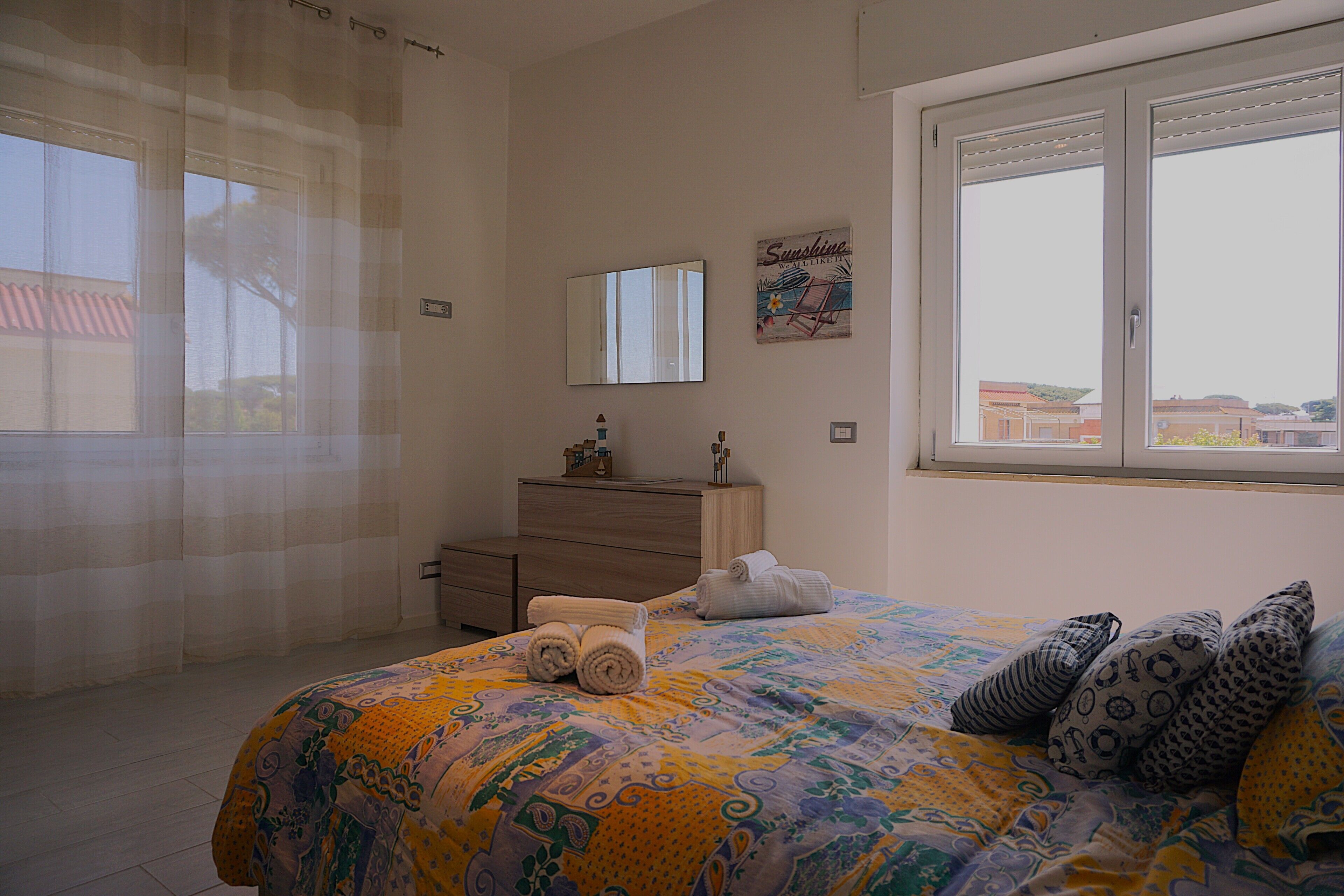 A bedroom with a bed, a dresser, a mirror, and a window with a view.