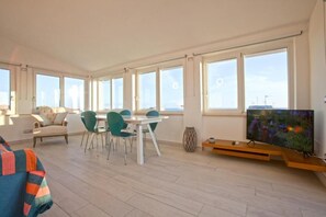 A spacious room with a dining area, a sofa, a television, and large windows.