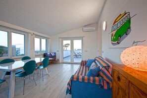 Una sala de estar moderna con un sofá, una mesa de comedor con sillas, un televisor y un ventanal grande.