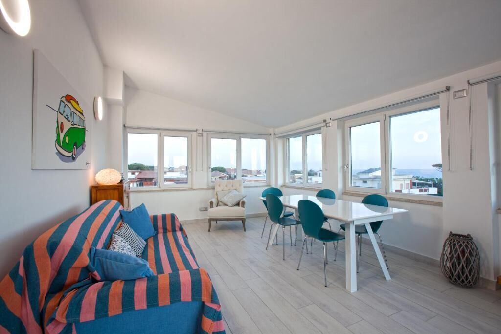 A bright room with a dining table and chairs, a sofa, and large windows offering a view.