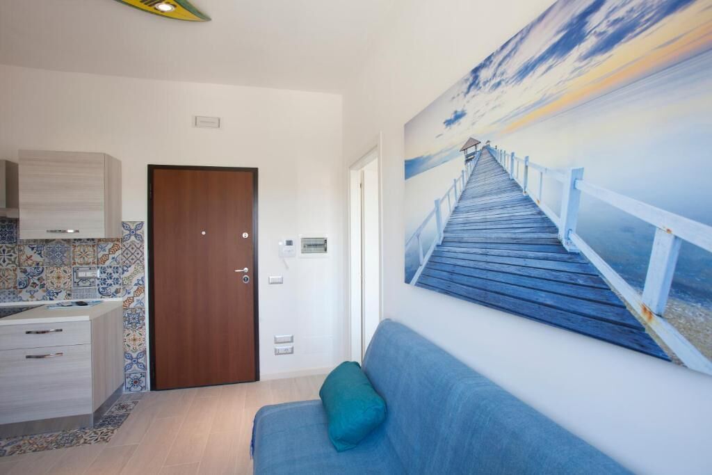 A room with a wooden door, a blue sofa with a teal pillow, a tiled backsplash, and a painting of a wooden staircase.