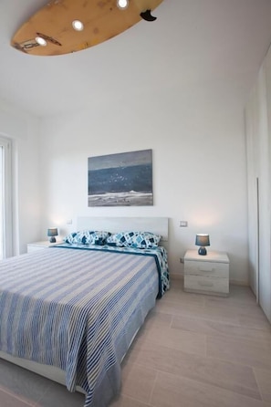 A bedroom with a bed, bedside tables, a nightstand, a ceiling light fixture, and a wall-mounted picture.