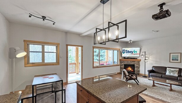 A modern kitchen with a central island, a dining area with a table, a fireplace, and a living room with a sofa.