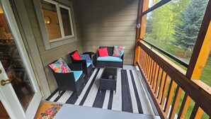 A covered porch with wicker furniture, a striped rug, and a view of a forest.