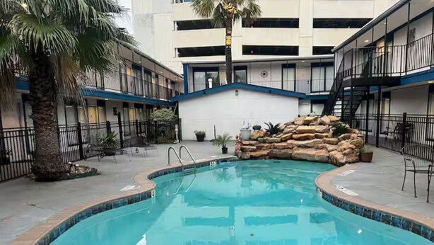 A swimming pool with a stone feature, surrounded by a building with balconies and a palm tree.