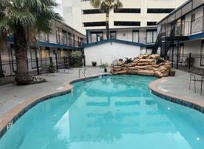 A swimming pool with a stone feature, surrounded by a building with balconies and a palm tree. - Galleria Parc Hotel & Apartment (Houston)