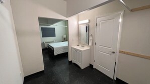 A hallway leading to a bedroom with a bed, a bathroom with a sink and mirror, and a door.