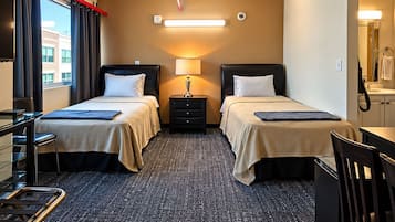 Habitación de hotel con dos camas, un escritorio, una silla, una lámpara y vista a un edificio.