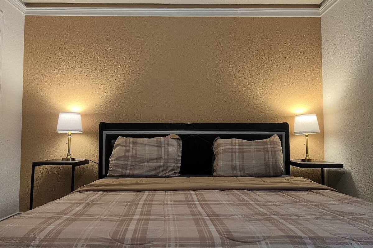 Una habitación de hotel con una cama, dos lámparas de noche y una pared con textura.