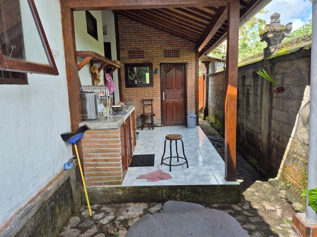 A covered outdoor area with a brick wall, a wooden door, a small stool, and a bench.