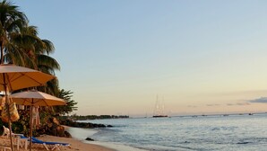 Ein Strand mit Sonnenschirmen, Liegestühlen und ruhigem Meer.