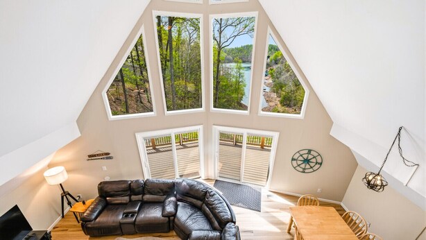 A loft bedroom with a large skylight, a curved black leather sofa, a wooden dining table, and a piano. - Old Rocky: 824 Deerfield Way (LaFollette)