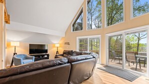 A modern living room with a large leather sofa, a flat-screen TV, and a dining area with outdoor seating. - Old Rocky: 824 Deerfield Way (LaFollette)