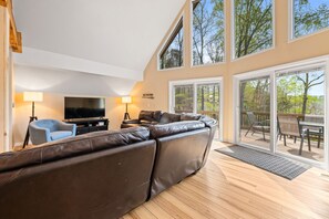 A modern living room with a large leather sofa, a flat-screen TV, and a dining area with outdoor seating. - Old Rocky: 824 Deerfield Way (LaFollette)