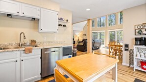 A modern kitchen with white cabinets, a stainless steel dishwasher, and a wooden dining table. - Old Rocky: 824 Deerfield Way (LaFollette)