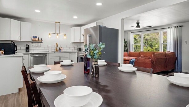 A modern kitchen with white cabinets, a central island with white plates, and a dining area with a brown sofa. - Sleeps 16 • Hot Tub • Egg Chairs • Pool Table • 4 bedroom • Near New River Gorge (Oak Hill)