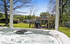 Ein Whirlpool mit Blick auf eine Rasenfläche, eine Laube und ein Haus im Hintergrund.