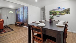 A dining area with a dark wooden table set for six, white plates, and a painting of a bridge on the wall. - Sleeps 16 • Hot Tub • Egg Chairs • Pool Table • 4 bedroom • Near New River Gorge (Oak Hill)