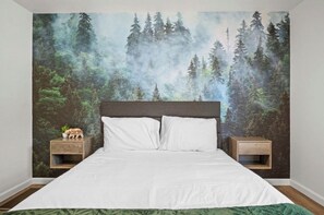Ein Schlafzimmer mit einem großen Bett, zwei Nachttischen und Wandteppich mit Waldmotiv.